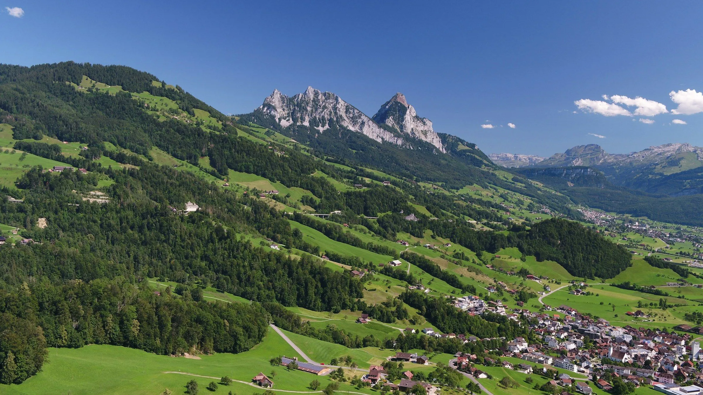 Talboden bei Steinen mit Dorf, Wiesen, Waldhängen und den Mythen